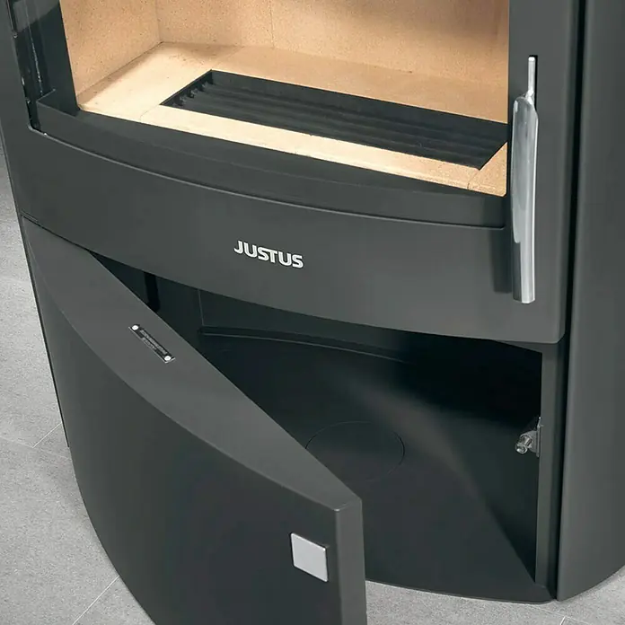 Justus Kaminofen Agero 2.0 - 7 kW, Raumheizvermögen: 144 m³, Material Verkleidung: Stahl, Schwarz - Nahaufnahme eines Justus Kaminofens mit geöffneter Tür, der Einblick ins Innere und auf Details des Ofens gewährt.