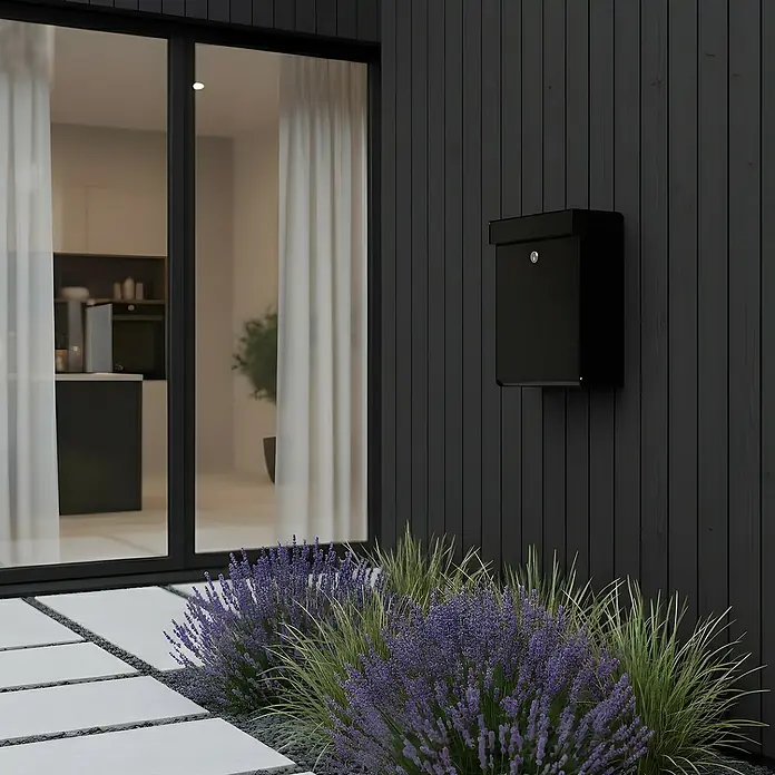 Allux Briefkasten Grundform - L x B x H: 180 x 345 x 440 mm, Schwarz, Stahl - Schwarzer Briefkasten an einer dunklen Holzfassade neben einem modernen Glaseingang.