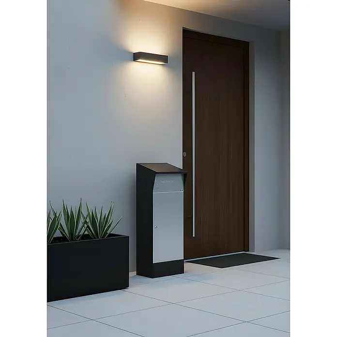 Allux Paketbox Björn mit LED - L x B x H: 365 x 400 x 1.100 mm, Schwarz / Grau, Stahl, Paketfach - Ein moderner, freistehender Briefkasten mit schwarzem Rahmen und silberner Frontplatte, an einem Eingang neben einer dunklen Holztür.