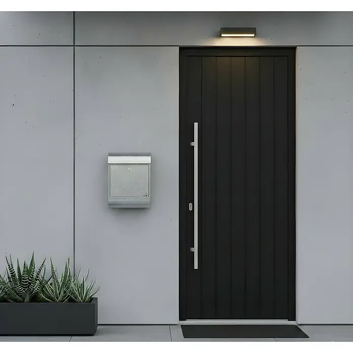 Allux Standbriefkasten 8900 - L x B x H: 160 x 340 x 500 mm, Silber, Stahl - Moderner Gebäudeeingang mit schwarzer Tür, silbernem Briefkasten und grünen Pflanzen.