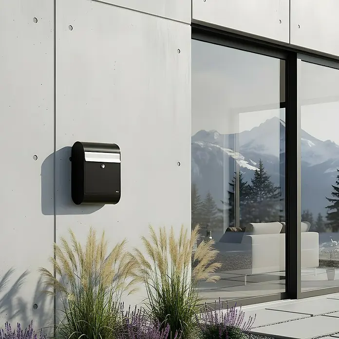 Allux Standbriefkasten 5000 - L x B x H: 160 x 320 x 460 mm, Schwarz / Silber, Stahl - Schwarzer Briefkasten an einer modernen Gebäudewand, der eine elegante und sichere Postempfangslösung bietet.