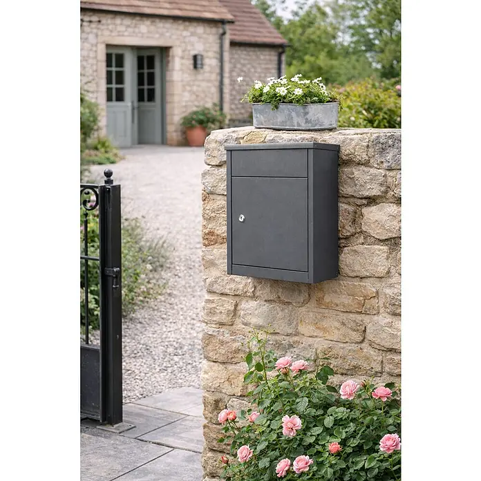 Allux Standbriefkasten 500 - L x B x H: 250 x 380 x 530 mm, Anthrazit, Stahl, Paketfach, Zylinderschloss - Dunkelgrauer Briefkasten an einer Steinmauer, integriert in ein natürliches Eingangsumfeld.