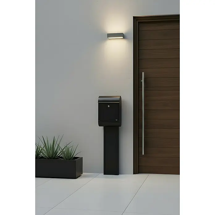 Allux Standbriefkasten 8900 - L x B x H: 160 x 340 x 500 mm, Schwarz, Stahl - Schwarzer freistehender Briefkasten in modernem Design, positioniert am Gebäudeeingang neben einer Holztür und einem Pflanzgefäß.
