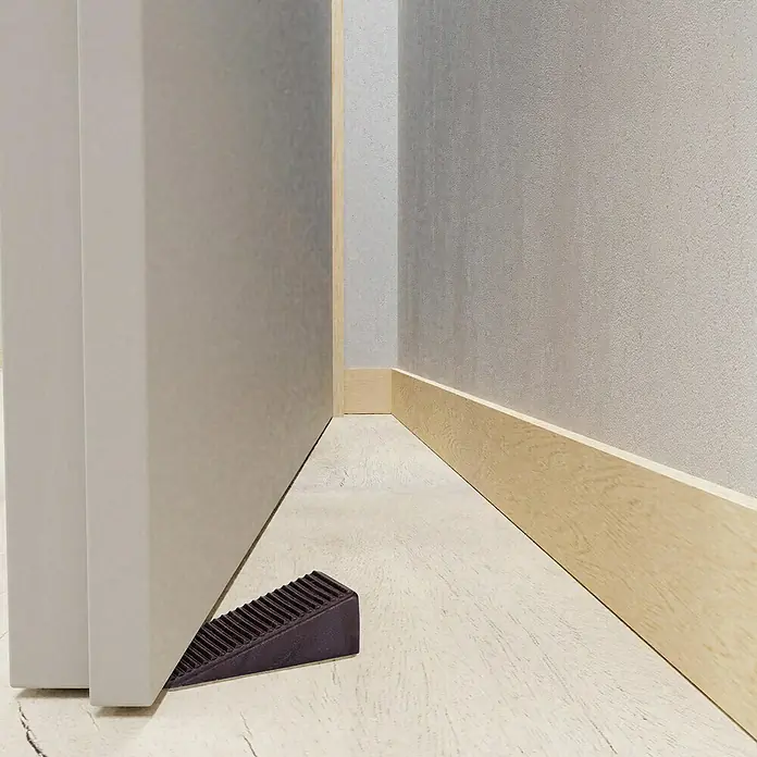 Walteco Türkeil - L x B x H: 50 x 15,5 x 19 mm, Braun, 4 Stk. - Dunkelbrauner, gerippter Türstopper hält eine hellgraue Tür auf einem hellen Holzboden offen.