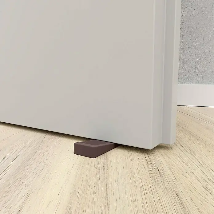 Walteco Türkeil - L x B x H: 50 x 15,5 x 19 mm, Braun, 4 Stk. - Dunkelbrauner, keilförmiger Türstopper mit Rillen oben, der eine helle Tür auf einem Holzboden offen hält.