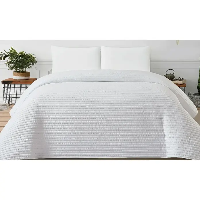 Colcha Farlow - 260 x 240 cm, 100% poliéster, Blanco - Colcha blanca acolchada sobre una cama con dos almohadas, resaltando su diseño texturizado.