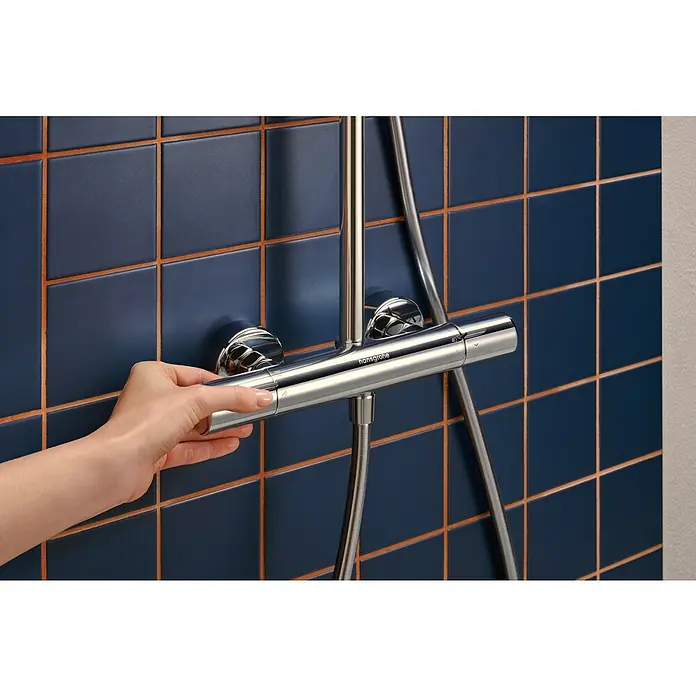 Hansgrohe Duschsystem Activera S - Lochabstand: 138 mm - 162 cm, Anzahl Strahlarten: 2 Stk., Chrom - Eine Hand bedient einen verchromten Hansgrohe Duschthermostat an einer blauen Fliesenwand.
