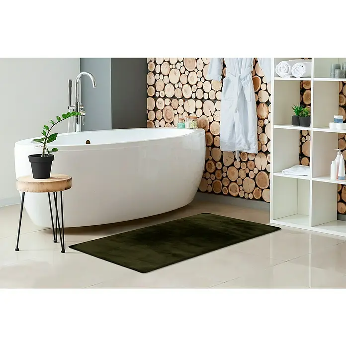 Badteppich Happy - 40 x 60 cm, Basil, 100% Polyester - Dunkelgrüne, rechteckige Badematte auf hellem Fliesenboden in einem modernen Badezimmer vor einer weißen Badewanne.