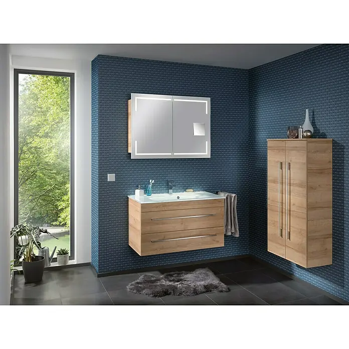 Camargue Stella Waschtischunterschrank - 99,4 x 48,8 x 55 cm, Ohne Beleuchtung, Berg Eiche - Badezimmer-Interieur mit einem Waschtischunterschrank aus Holz, einem Spiegelschrank mit Beleuchtung und einem hochhängenden Schrank an einer blau gemusterten Wand.