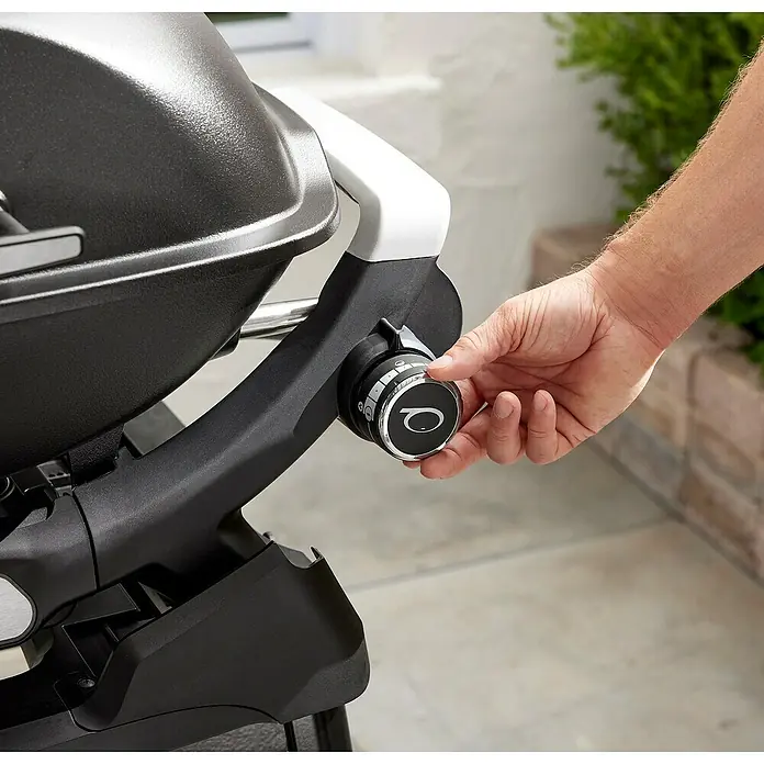 Weber Gasgrill Q 2200 N - Grillfläche (B x T): 56 x 41 cm, 4,11 kW, Anzahl Brenner: 1 Stk. - Eine Hand verstellt einen silbernen und schwarzen Bedienknopf an einem strukturierten schwarzen Grill, um die Temperatur einzustellen.