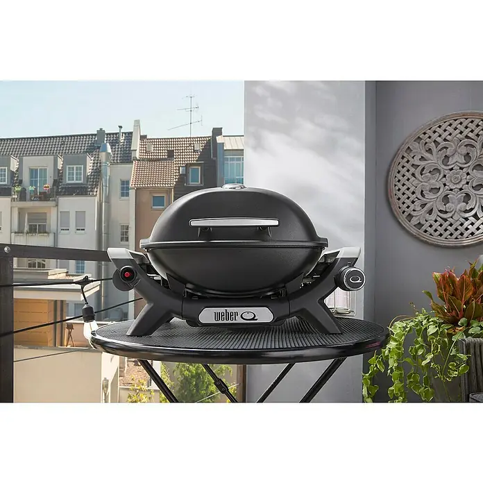 Weber Gasgrill Q 1100 N - Grillfläche (B x T): 45 x 36 cm, 2,94 kW, Anzahl Brenner: 1 Stk. - Ein schwarzer, kuppelförmiger Weber Q Grill steht auf einem schwarzen Balkontisch, bereit zum urbanen Grillen.