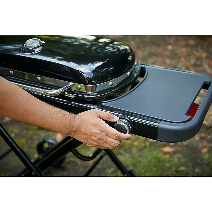 Weber Gasgrill Traveler - Grillfläche (B x T): 63 x 34 cm, 3,8 kW, Anzahl Brenner: 1 Stk. - Hand dreht einen Bedienknopf an einem schwarzen Gasgrill mit Chromdetails.