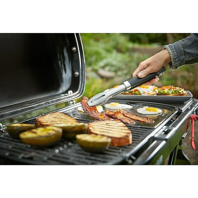 Weber Gasgrill Traveler - Grillfläche (B x T): 63 x 34 cm, 3,8 kW, Anzahl Brenner: 1 Stk. - Eine Person wendet Speck mit einer Zange auf einem schwarzen Outdoor-Grill, auf dem Eier, Speck, gegrillte Avocado und Brot zubereitet werden.