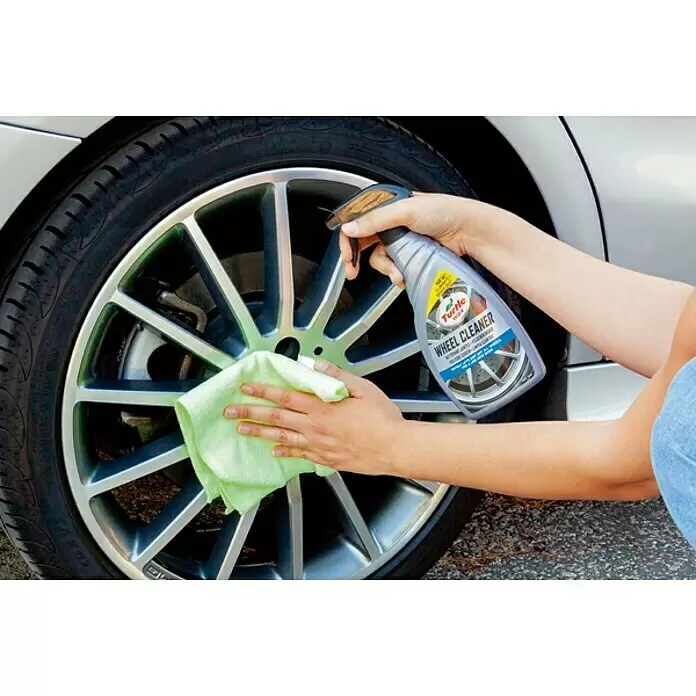 Turtle Wax Limpiador de llantas - 500 ml - Manos rocían limpiador de llantas Turtle Wax sobre una llanta de aleación plateada y la limpian con un paño verde.
