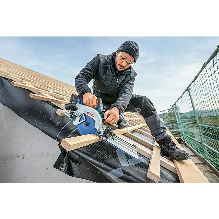 Bosch Professional Führungsschiene FSN 440 X - L x B x H: 783 x 228 x 49 mm - Mann schneidet mit einer blauen und silbernen Bosch Kreissäge ein Holzbrett auf einer Dachkonstruktion.