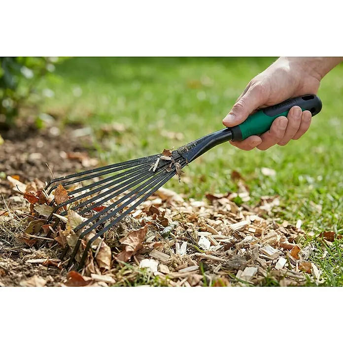 Gardol Hand-Kleinfeger - Arbeitsbreite: 12,5 cm, Anzahl Zinken: 9, Kurzstiel - Eine Hand hält einen schwarzen und grünen kleinen Gartenrechen und harkt trockene Blätter und Holzspäne vom Boden.