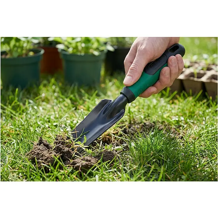 Gardol Hand-Unkrautstecher - Arbeitsbreite: 30 mm, Kurzstiel - Hand hält eine schwarze und grüne Handschaufel, die im Garten Erde und Gras umgräbt.