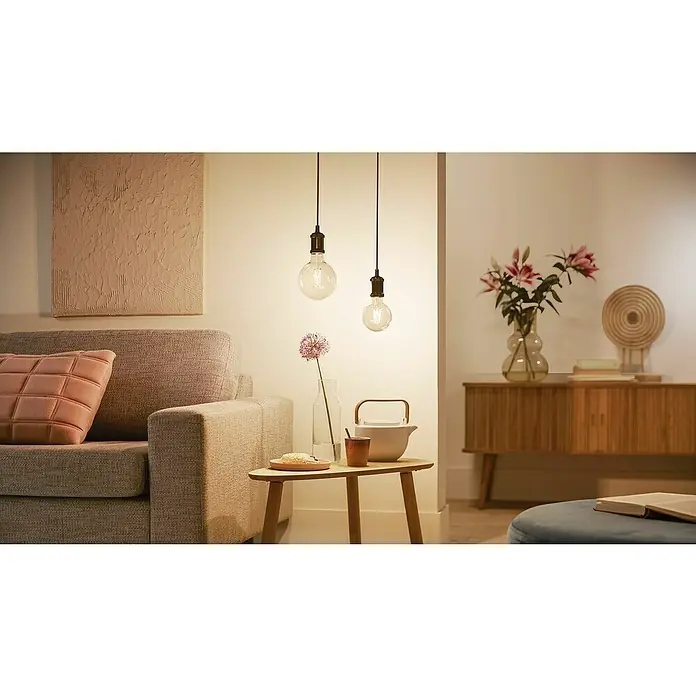 WiZ Smart-LED-Lampe G125 - E27, Dimmbar, Warmweiß, 806 lm, 7 W, 1 Stk. - Zwei klare Pendelleuchten erhellen ein gemütliches Wohnzimmer mit warmem Licht.