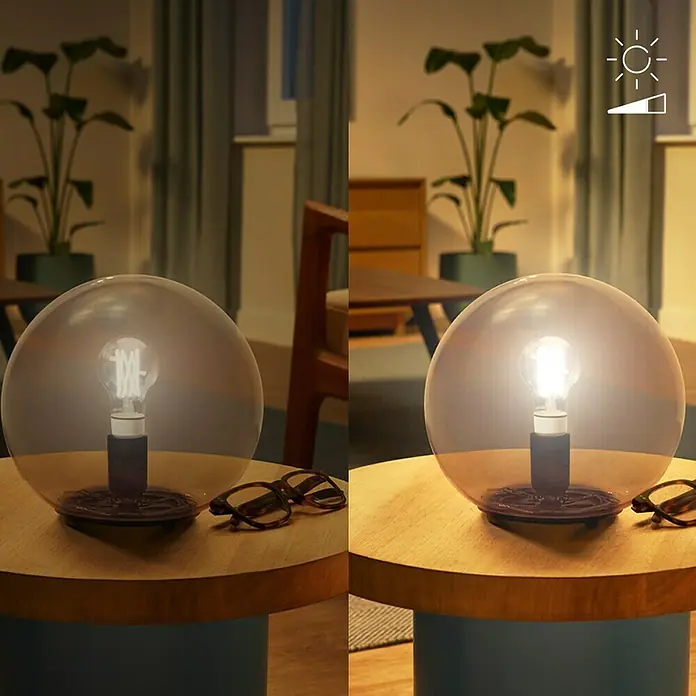 Philips Wiz Smart-LED-Lampe - E27, Dimmbar, Neutralweiß, 903 lm, 8 W, 1 Stk. - Tischlampe mit Rauchglas-Kugelschirm und sichtbarer Glühbirne, ausgeschaltet und beleuchtet auf einem Holztisch im Wohnzimmer.