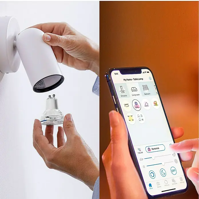 Philips Wiz Smart-LED-Lampe - GU10, Dimmbar, RGBW, 400 lm, 4,7 W, 1 Stk. - Eine Person installiert eine smarte GU10 LED-Birne in einen weißen Strahler, während eine andere Person smarte Lichter über eine Smartphone-App steuert.