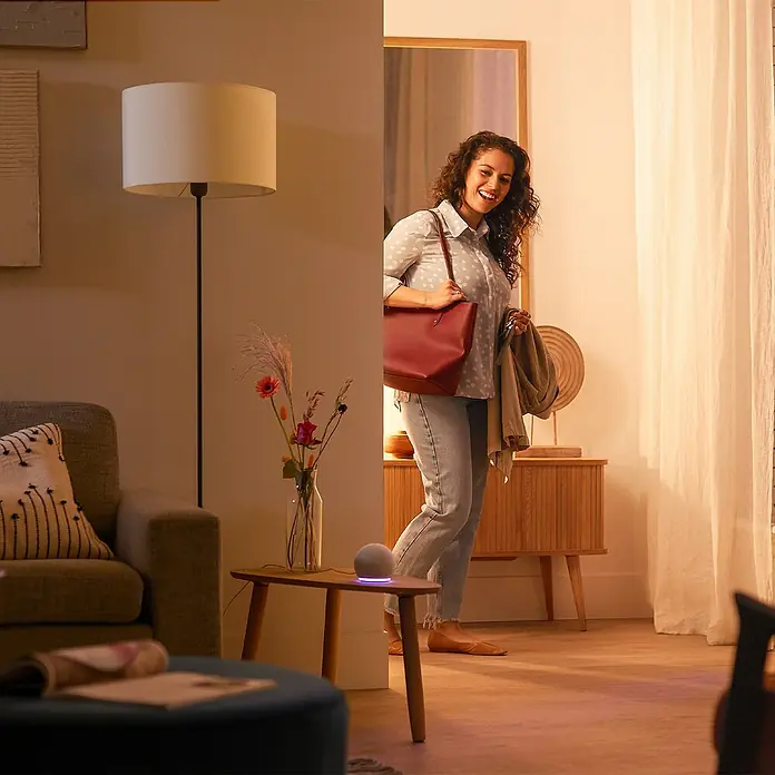 Philips Wiz Smart-LED-Lampe matter - E27, Dimmbar, RGBW, 1.521 lm, 13 W, 1 Stk. - Weißer kugelförmiger Smart Speaker mit violettem Lichtring auf einem Holzbeistelltisch in einem modernen Wohnraum.