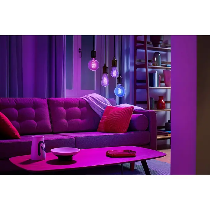 Philips Wiz Smart-LED-Lampe - E27, Dimmbar, RGBW, 470 lm, 6,3 W, 1 Stk. - Vier smarte Glühbirnen hängen in einem Wohnzimmer und beleuchten den Raum in Lila, Pink und Blau.
