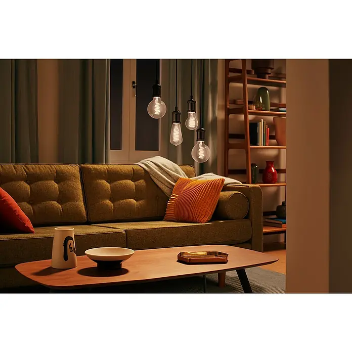 Philips Wiz Smart-LED-Lampe - E27, Dimmbar, RGBW, 470 lm, 6,3 W, 1 Stk. - Fünf hängende LED-Glühbirnen mit warmen Spiralfilamenten beleuchten ein gemütliches Wohnzimmer mit Sofa und Couchtisch.