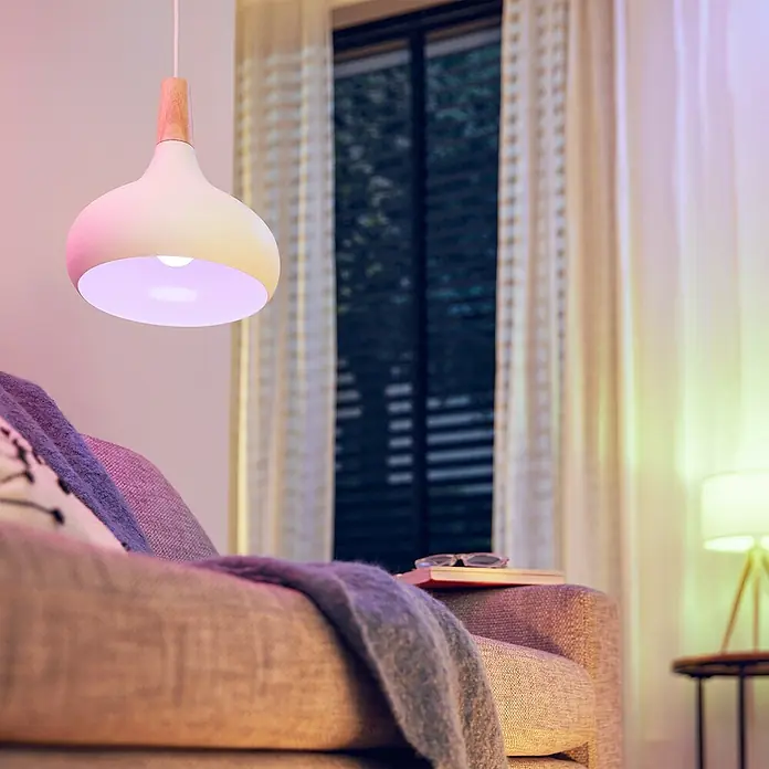Philips Wiz Smart-LED-Lampe matter - E27, Dimmbar, RGBW, 1.521 lm, 13 W, 1 Stk. - Weiße Pendelleuchte aus Metall mit Holzdetails, beleuchtet ein Wohnzimmer mit violettem Licht.