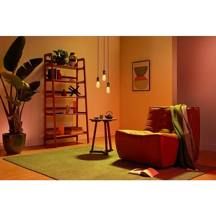 Philips Wiz Smart-LED-Lampe Edison - E27, Dimmbar, RGBW, 470 lm, 6,3 W, 1 Stk. - Gemütliches Wohnzimmer mit braunem Sessel, Holzregal, Pflanze und warmen Hängelampen für eine einladende Atmosphäre.