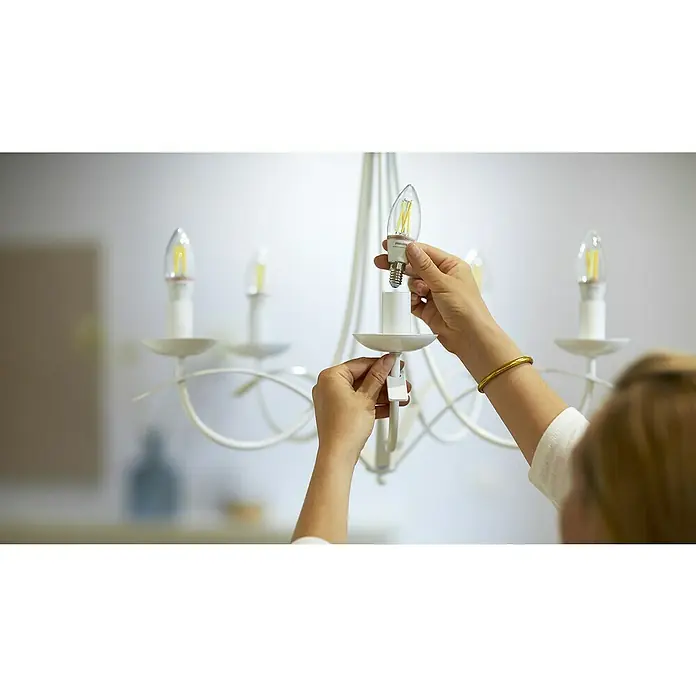 Philips Wiz Smart-LED-Lampe - E14, Dimmbar, Neutralweiß, 470 lm, 4,9 W, 1 Stk. - Hände montieren eine klare Philips WiZ LED-Birne mit gelben Filamenten in einen weißen Kronleuchter.