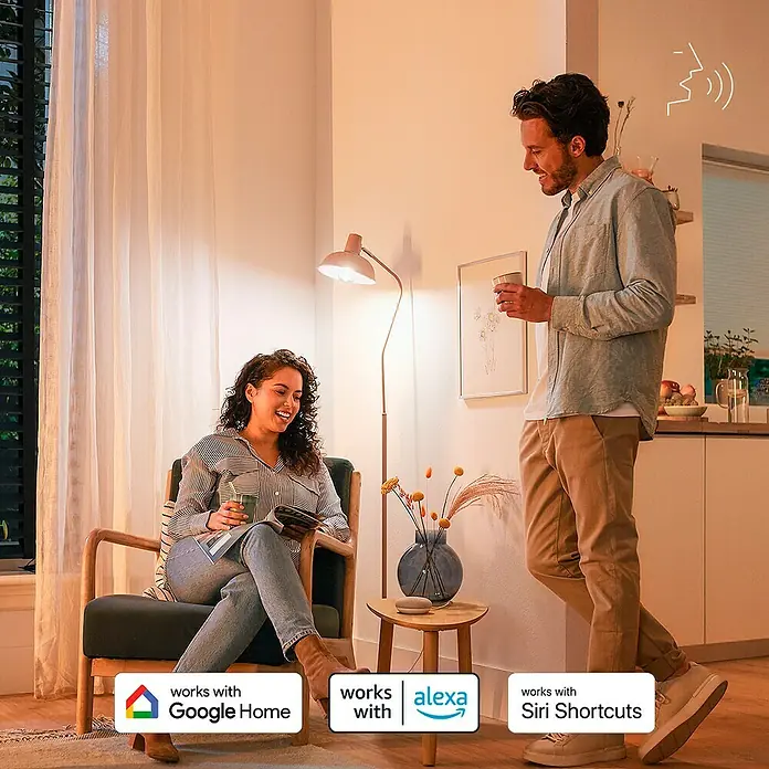 Philips Wiz Smart-LED-Lampe matter - E27, Dimmbarkeit: Dimmbar, Neutralweiß, 1.055 lm, 11 W - Kleiner beiger Smart Speaker auf einem Holztisch, integriert in ein Smart Home System, während Personen interagieren.