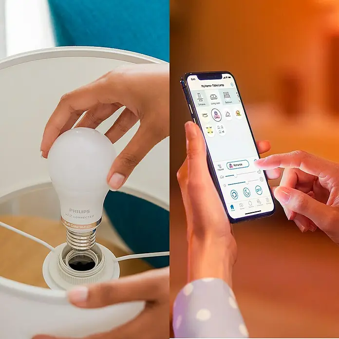 Philips Wiz Smart-LED-Lampe matter - E27, Dimmbarkeit: Dimmbar, Neutralweiß, 1.055 lm, 11 W - Eine Hand installiert eine Philips WiZ LED Smart-Glühbirne; eine andere Hand steuert Einstellungen, inkl. "Romance"-Modus, per Smartphone-App.