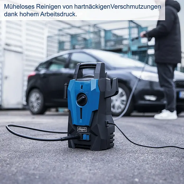 Scheppach Hochdruckreiniger SHD110 - 1.400 W, Max. Druck: 110 bar, Fördermenge: 390 l/h - Blauer und schwarzer Scheppach Hochdruckreiniger auf Asphalt, im Hintergrund reinigt eine Person ein Auto.