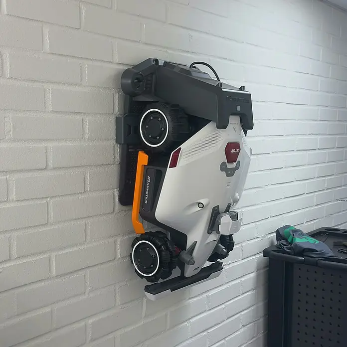 Grimsholm Green Wandhalterung für Rasenmäher - L x B x H: 100 x 5.650 x 1.750 mm, Mammotion Luba 2 AWD - Weiß-graues Robotikgerät mit orangefarbenen Akzenten und großen Rädern, vertikal zur Aufbewahrung montiert.