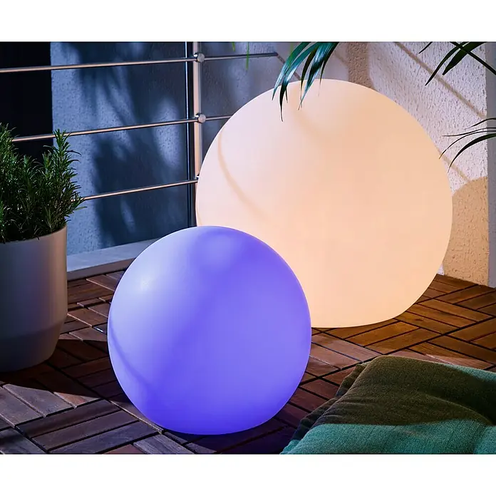 New Garden Solar-Dekoleuchte Buly - Durchmesser: 30 cm, IP65 - Zwei leuchtende kugelförmige Außenlampen, eine cremefarbene und eine violette, beleuchten eine Holzterrasse mit Pflanze und Decke.
