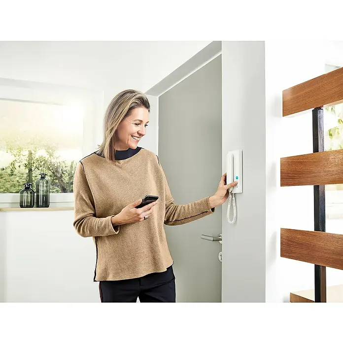 Siedle Türsprechanlage Compact SET CA 812-4 E/W - 4 Personen-Haushalt, Weiß, Silber - Frau bedient ein weißes Wand-Gegensprechanlage-System mit einem Smartphone.