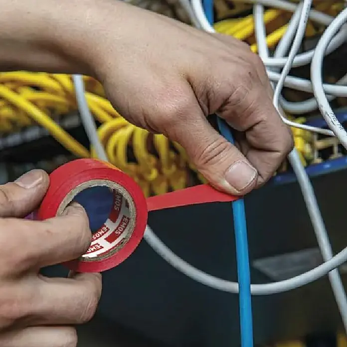 Emos Isolierband F61512 - Schwarz, L x B: 10 m x 15 mm - Hände wickeln rotes Isolierband um ein blaues Kabel, inmitten anderer Kabel.