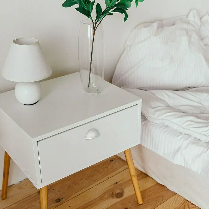 Rei Möbelgriff - Lochabstand: 64 mm, Sonstige, Chrom, L x B x H: 80 x 29 x 25 mm - Ein weißer Nachttisch mit Holzbeinen und silbernem Schubladengriff neben einem Bett, auf dem eine Lampe und eine Vase stehen.