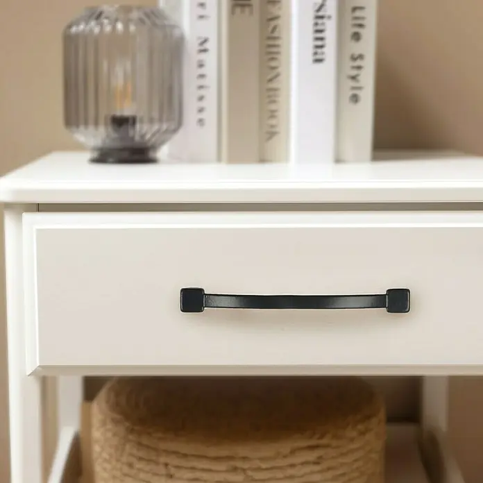 Rei Möbelgriff - Lochabstand: 96 mm, Sonstige, Schwarz, L x B x H: 103 x 10 x 19 mm - Weißer Nachttisch mit schwarzem Schubladengriff. Oben sind Bücher und eine Lampe, unten ein geflochtener Korb.