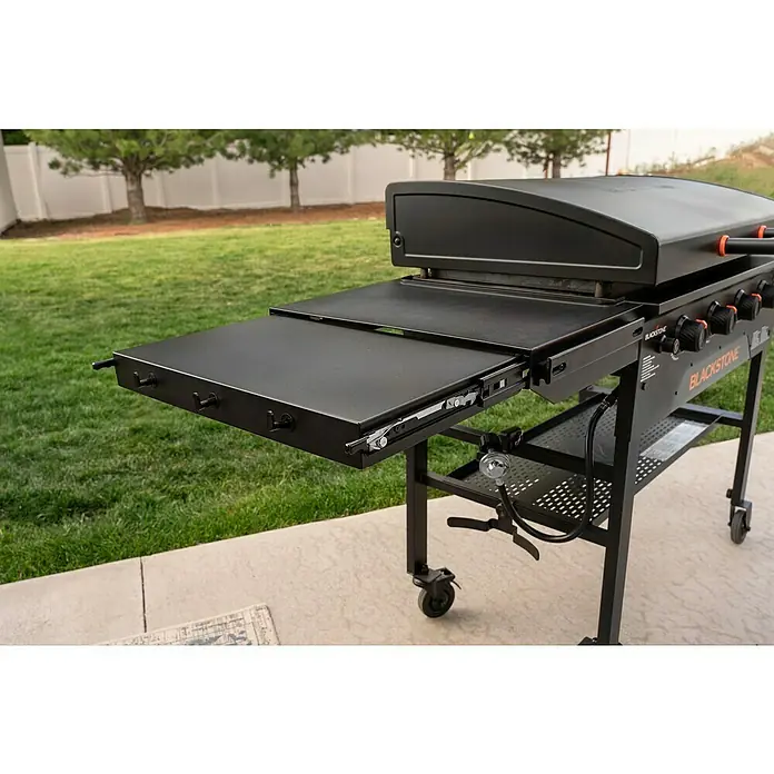Blackstone Plancha Grill - Superficie de la parrilla (An x Pr): 91 x 55 cm, Negro, Número de quemadores: 4 ud. - Plancha Blackstone negra con estante lateral de metal negro extendido, mostrando ganchos y mecanismo deslizante.