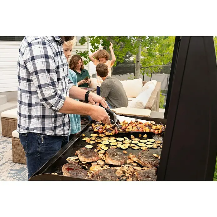Blackstone Plancha Grill - Superficie de la parrilla (An x Pr): 91 x 55 cm, Negro, Número de quemadores: 4 ud. - Hombre asando filetes, verduras y champiñones en una gran plancha exterior, rodeado de familia.
