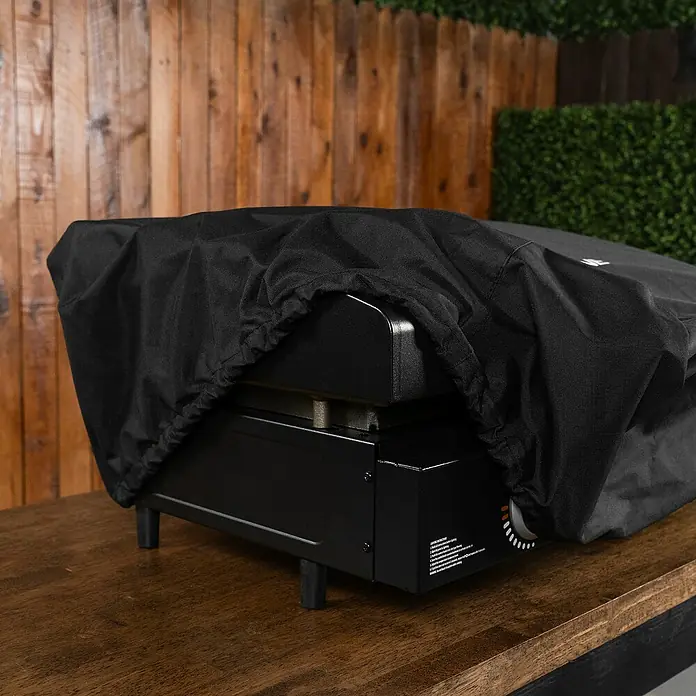 Blackstone Grill-Schutzhülle - Passend für: Blackstone Plancha-Grill 22", Polyester - Schwarze Grillplatte mit schwarzer Schutzhülle aus Stoff auf einer Holzoberfläche.