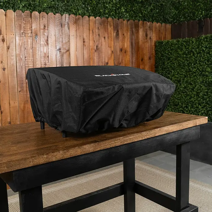 Blackstone Grill-Schutzhülle - Passend für: Blackstone Plancha-Grill 22", Polyester - Eine schwarze Blackstone Schutzhülle für eine Grillplatte auf einem Holztisch im Freien.