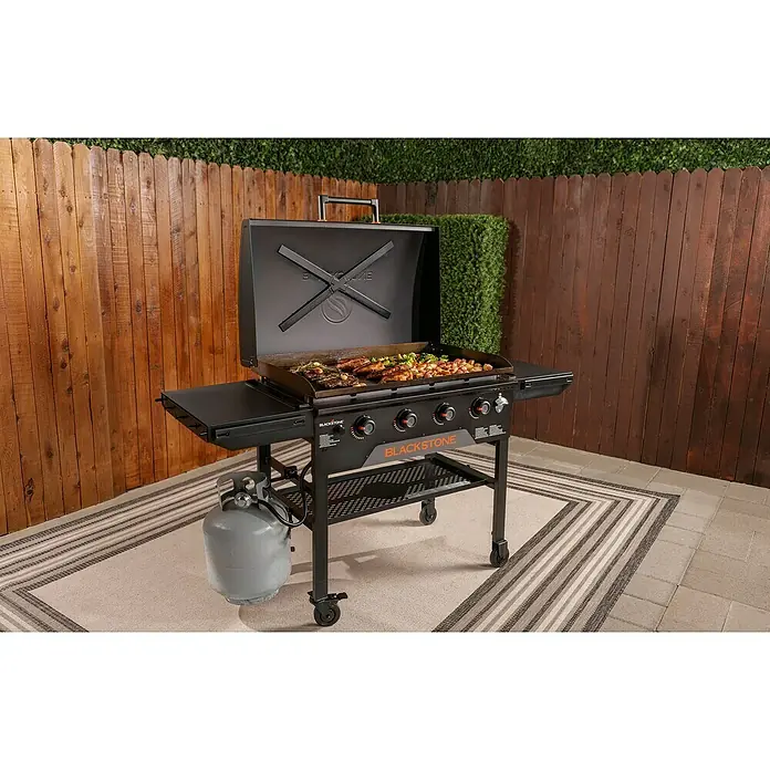 Blackstone Plancha Grill - Superficie de la parrilla (An x Pr): 91 x 55 cm, Negro, Número de quemadores: 4 ud. - Plancha Blackstone negra con comida cocinándose en superficie metálica, tanque de propano, al aire libre.