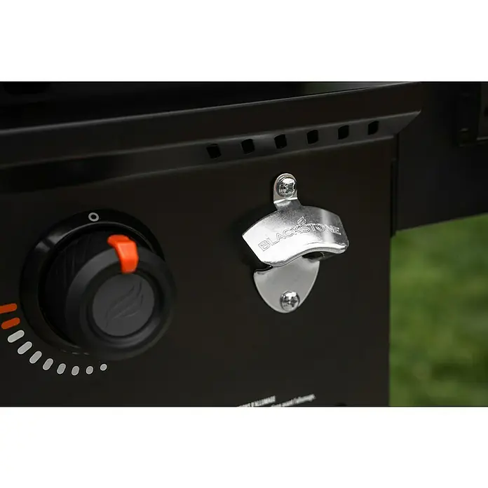 Blackstone Plancha Grill - Superficie de la parrilla (An x Pr): 91 x 55 cm, Negro, Número de quemadores: 4 ud. - Primer plano de una plancha negra con un mando de control con indicador naranja y un abridor de botellas Blackstone plateado y grabado.
