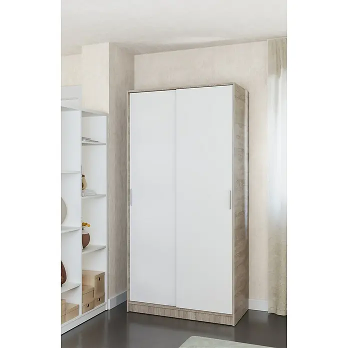 Meka Block Armario de puertas correderas K-511 - L x An x Al: 50 x 100 x 200 cm, Blanco Liso/Roble Cortez - Armario con puertas correderas blancas y marco efecto madera clara en una habitación moderna.
