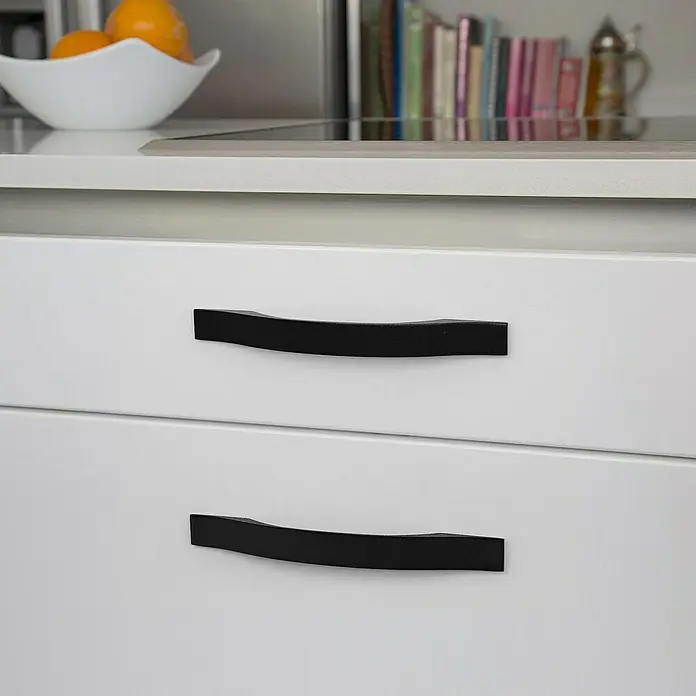 Rei Möbelgriff - Lochabstand: 128 mm, Aluminium, Schwarz, Rustikal - Zwei matte schwarze, geschwungene Schubladengriffe an weißen Küchenschränken.