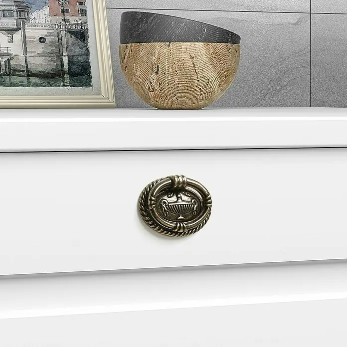 Rei Möbelgriff - Lochabstand: 32 mm, Sonstige, Antikes Messing - Dekorativer antiker bronzefarbener Fallgriff mit Urnenmotiv an einer weißen Schublade.