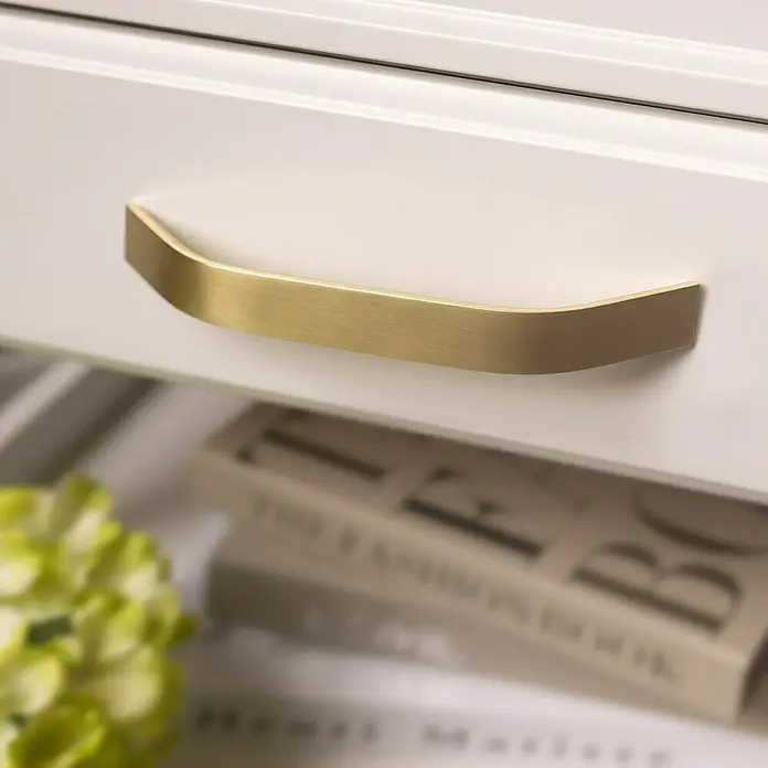 Rei Möbelgriff - Lochabstand: 160 mm, Aluminium, Antikes Messing, Gebogen - Elegante, gebürstete goldene Griffleiste an einer hellen Schublade.
