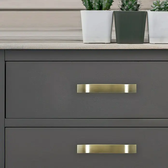 Rei Möbelgriff - Lochabstand: 160 mm, Aluminium, Antikes Messing, Gebogen - Zwei elegante Messing-Schubladengriffe an einem dunkelgrauen Zweischubladen-Schrank.
